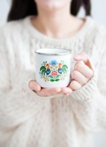 Image of person with black hair and white sweater holding a tea cup with flowers.